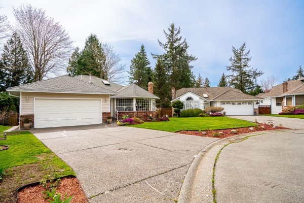 Front view of a beige house with a white garage door and manicured lawn. - 13560 15a Avenue, Surrey