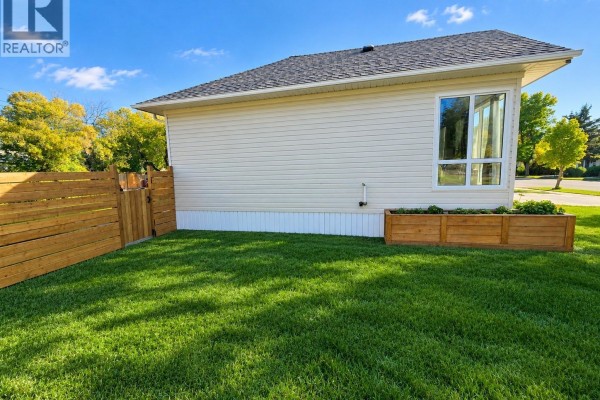 Backyard view of a cream-colored house with a horizontal wood fence and a raised planter. - 136 10th Street Ne, Weyburn