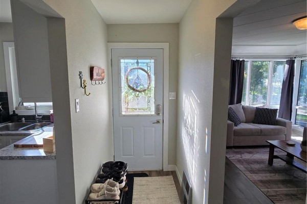 Entranceway showing a white door, shoe rack, and view into a living area with a couch. - 136 10th Street Ne, Weyburn