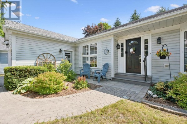 Close-up of the bungalow's front entrance with a gray walkway, two blue chairs, and landscaping. - 136 Bristlecone Crescent, Centre Wellington