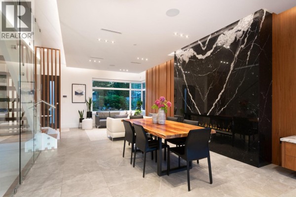Open-concept dining and living area with a live-edge wood table, black chairs, and marble fireplace. - 136 E 61st Avenue, Vancouver