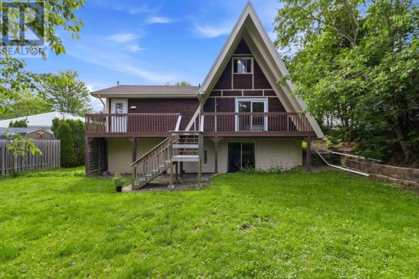 Rear exterior of an A-frame house with a wooden deck and green lawn. - 136 Empire Street, Bridgewater