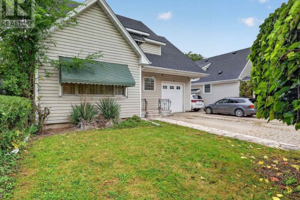 Side view of the house showing beige siding, green awning, and a paved driveway with cars. - 136 Highland Avenue, St  Catharines