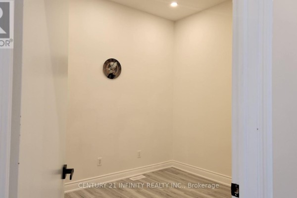 Small, empty room with neutral walls, gray flooring, and a circular decorative piece on the wall. - 136 Simcoe Street S, Oshawa