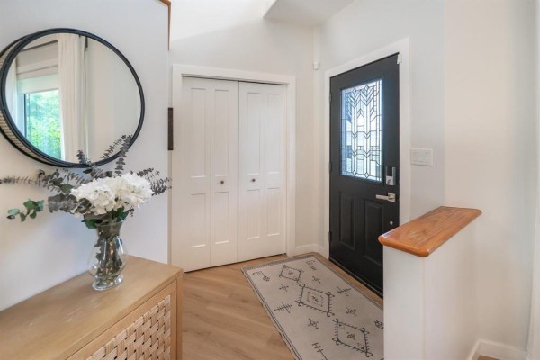Interior foyer with a black front door, light wood laminate flooring, and a round wall mirror. - 136 Swinford Way, Winnipeg