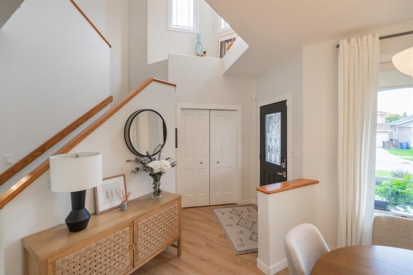 Foyer and staircase with light wood laminate flooring, white walls, wooden railings, and a decorative console table. - 136 Swinford Way, Winnipeg