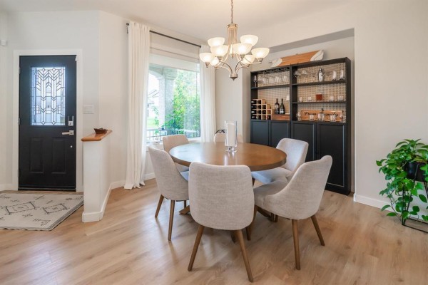 Dining area with an oval wooden table, six grey upholstered chairs, and a black wall-mounted cabinet. - 136 Swinford Way, Winnipeg