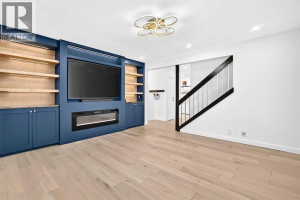 Living room with a large blue built-in entertainment unit, electric fireplace, and hardwood floors. - 136 Templehill Drive Ne, Calgary