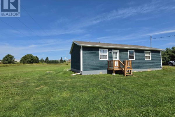 A green bungalow sits in a large grassy field under a blue sky. - 1366b Pownal Road, Alexandra