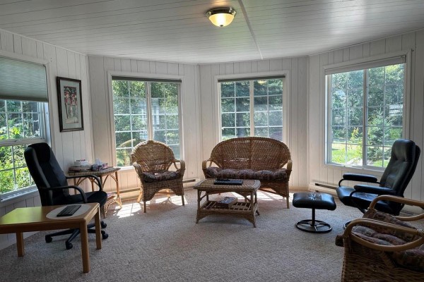 Living room with wicker furniture, office chair, and large windows. - 1367 Queens Street, Birtle