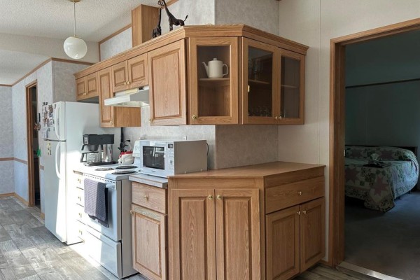 Kitchen with white appliances, wooden cabinets, and a view into a bedroom. - 1367 Queens Street, Birtle
