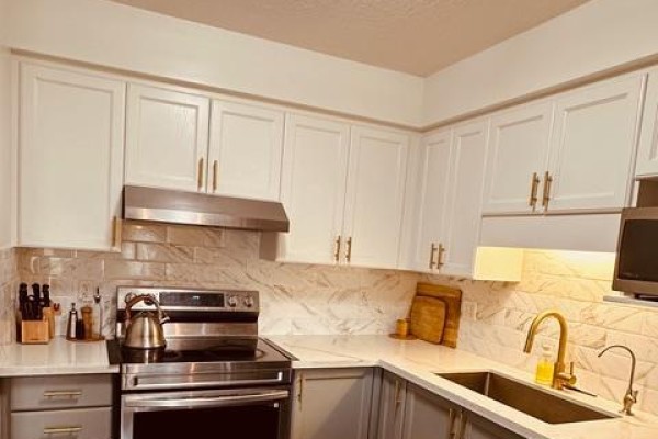 Kitchen corner with white cabinets, grey base cabinets, stainless steel stove, and marble backsplash. - 1369 Countrystone Drive, Kitchener