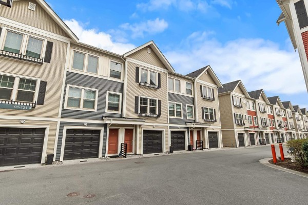 A living room with a sectional sofa, coffee table, rug, and an open-concept kitchen. - 137 32633 Simon Avenue, Abbotsford