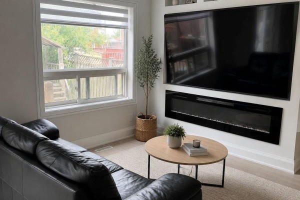 Living room with black leather sofa, electric fireplace, large TV, and window view. - 137 Hudson Crescent, Bradford West Gwillimbury