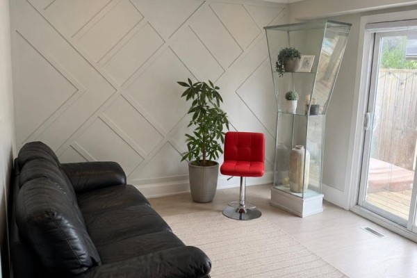 Living room with black sofa, decorative wall paneling, glass display cabinet, and sliding glass door. - 137 Hudson Crescent, Bradford West Gwillimbury