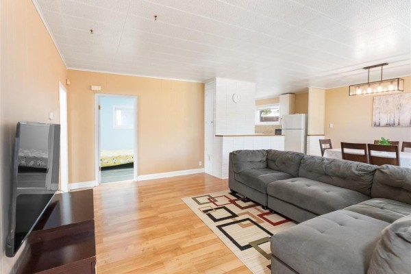Living room with a large sectional sofa, wood floors, and an open view to the dining and kitchen areas. - 137 Kilbride Avenue, Winnipeg