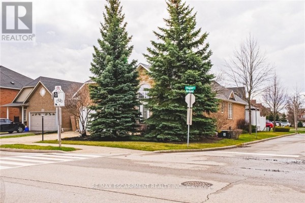 Residential street view with a brick house, large evergreen trees, and a street sign. - 137 Pinehill Drive, Hamilton