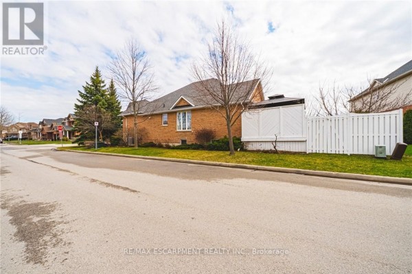 Side view of a brick house with a white picket fence and surrounding greenery. - 137 Pinehill Drive, Hamilton