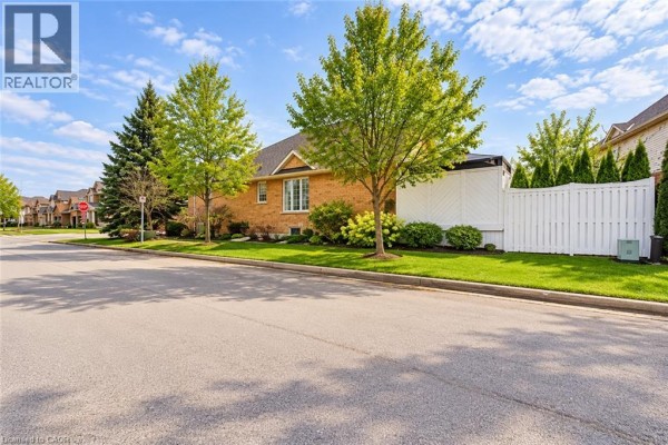 Side view of a brick house with landscaping and a white vinyl fence. - 137 Pinehill Drive, Stoney Creek