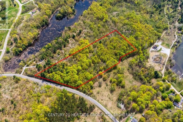 Aerial view of a treed lot outlined in red, beside a paved road and water. - 1371 Crow Lake Road, North Frontenac