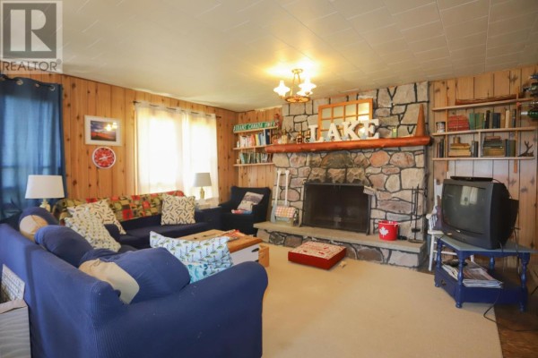 Living room with a stone fireplace, wood paneling, blue sofas, and shelves of books. - 1371 Sailors Encampment Dr, Richards Landing