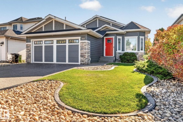 Front view of a grey house with a red door, stone details, and a manicured lawn with stone landscaping. - 13725 - 131b Avenue Nw, Edmonton