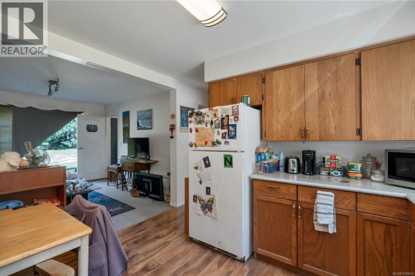 Kitchen with wood cabinets, white refrigerator, and view of living area. - 1376 Hooley Rd, Quadra Island