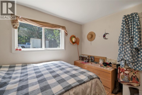Bedroom with a bed, dresser, and window overlooking trees and a building. - 1376 Hooley Rd, Quadra Island