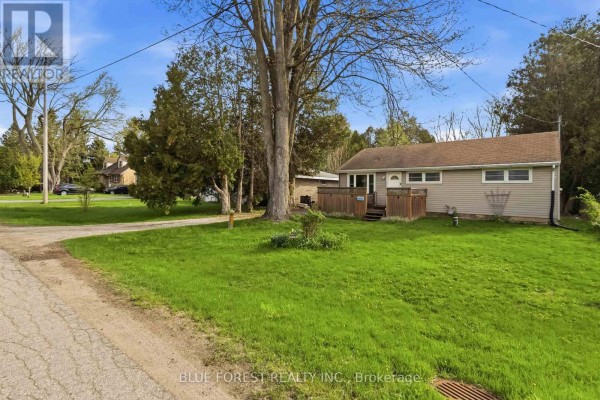 Side view of a beige bungalow with a wooden deck and a large tree in the yard. - 1376 Kostis Avenue, London East