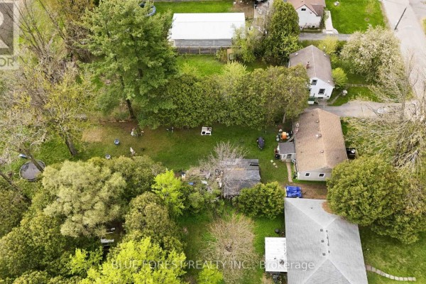 Gravel driveway leading to a beige bungalow with a wooden deck and surrounding green lawn. - 1376 Kostis Avenue, London East