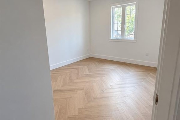 Empty bedroom with white walls, a large window, and light wood herringbone flooring. - 1377 Drouillard Unit# 2, Windsor