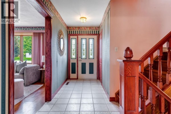 Interior hallway with a staircase, patterned wallpaper, and a glass-paneled front door. - 1379 Oxford Ave, Kingsville