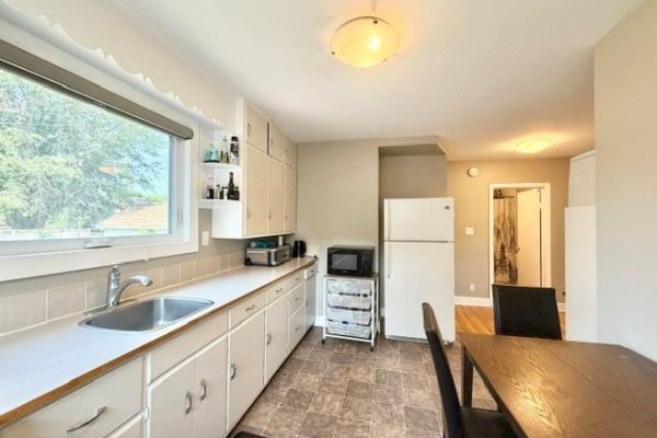 Kitchen with white cabinets, beige countertops, and a sink. A white refrigerator and a microwave are visible. A dining area is in the background. - 138 26th Street, Brandon