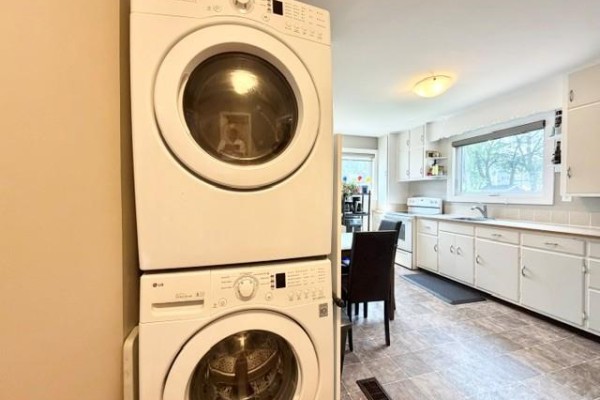 Stacked white LG washer and dryer in the corner of a beige-walled room. The kitchen and dining area are visible in the background. - 138 26th Street, Brandon