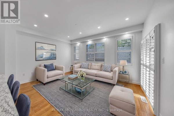 Living room with beige sofa, chairs, glass coffee table, and white shutters. - 138 Angus Drive, Ajax