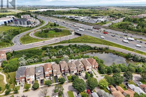 Aerial view of a suburban street with townhouses next to a pond and highway. - 138 Angus Drive, Ajax