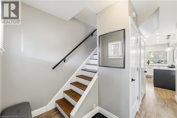 Interior view of a staircase, hallway, and glimpse into a kitchen with an island. - 138 Cameron Avenue N, Hamilton