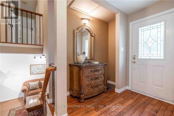 Entryway with hardwood floors, ornate dresser, mirror, and staircase. - 138 Judith Crescent, Hamilton
