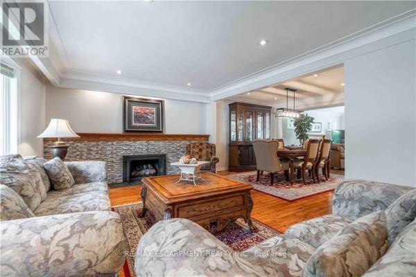 Living room with floral sofas, stone fireplace, and view of dining room. - 138 Judith Crescent, Hamilton