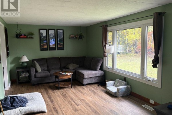 Living room with dark grey sectional sofa, round coffee table, hardwood floors, and large window overlooking yard. - 138 Road 5 Road S, Thunder Bay