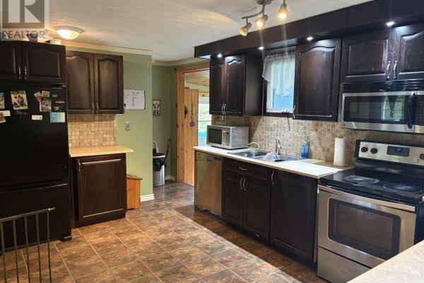 Dark wood kitchen cabinets, stainless steel appliances including refrigerator and stove, tile backsplash, and tiled floor. - 138 Road 5 Road S, Thunder Bay