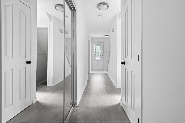 Hallway with white doors, mirrored closet doors, and grey wood-look flooring. - 138 Rue Bourgeau N., Gatineau