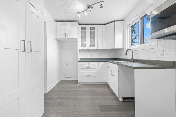 White kitchen with grey countertops, white cabinets, and a window overlooking trees and sky. - 138 Rue Bourgeau N., Gatineau