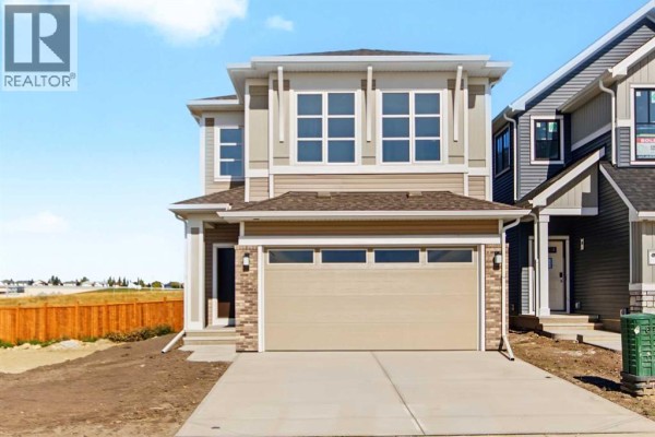 Front exterior of a modern two-story house with a beige and tan facade and a double garage. - 138 Silver Spruce Road Sw, Calgary