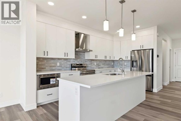 Modern white kitchen with a large island, stainless steel appliances, and grey subway tile backsplash. - 138 Silver Spruce Road Sw, Calgary