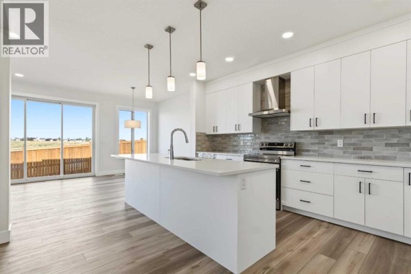 Open concept kitchen and living area with a large island, white cabinets, and sliding glass doors. - 138 Silver Spruce Road Sw, Calgary
