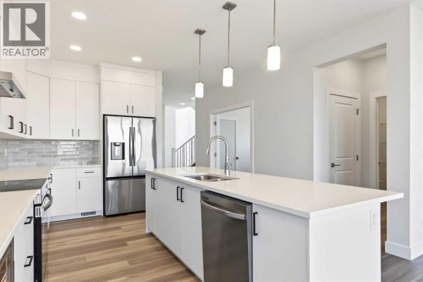 White kitchen with stainless steel refrigerator, dishwasher, and a large island with a sink. - 138 Silver Spruce Road Sw, Calgary