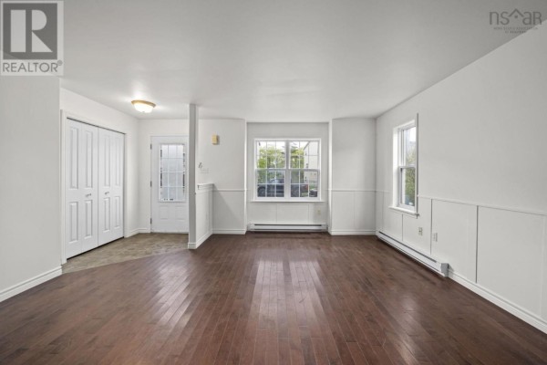 Living area with dark hardwood floors, white paneled walls, and view of staircase and doors. - 138 Transom Drive, Halifax