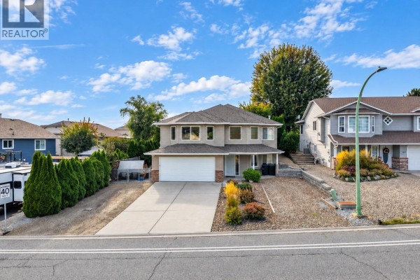 Front view of a beige house with a concrete driveway and landscaped yard. - 1380 Loseth Drive, Kelowna