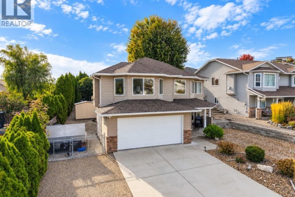 Side view of a beige house with a white garage door and green trees. - 1380 Loseth Drive, Kelowna